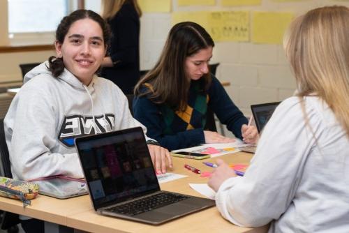 A student in a classroom of other students smiles at the camera