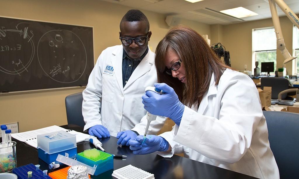 two students in lab coast and gloves work in a pharmacy lab