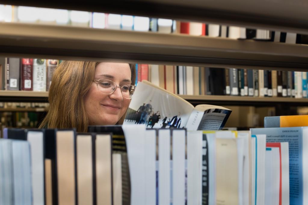 A U N E students read a book behind a bookshelf