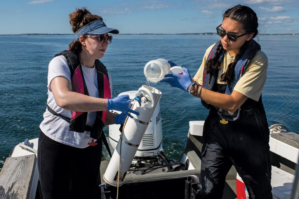 Two marine science students filling a sampling container with ocean water