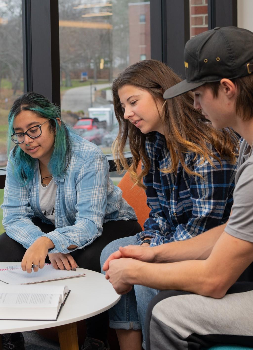 Three students sit at a table and read class notes off a notebook